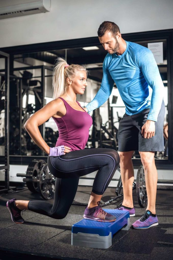 Personal trainer assisting client with step lunge exercise in Congleton gym