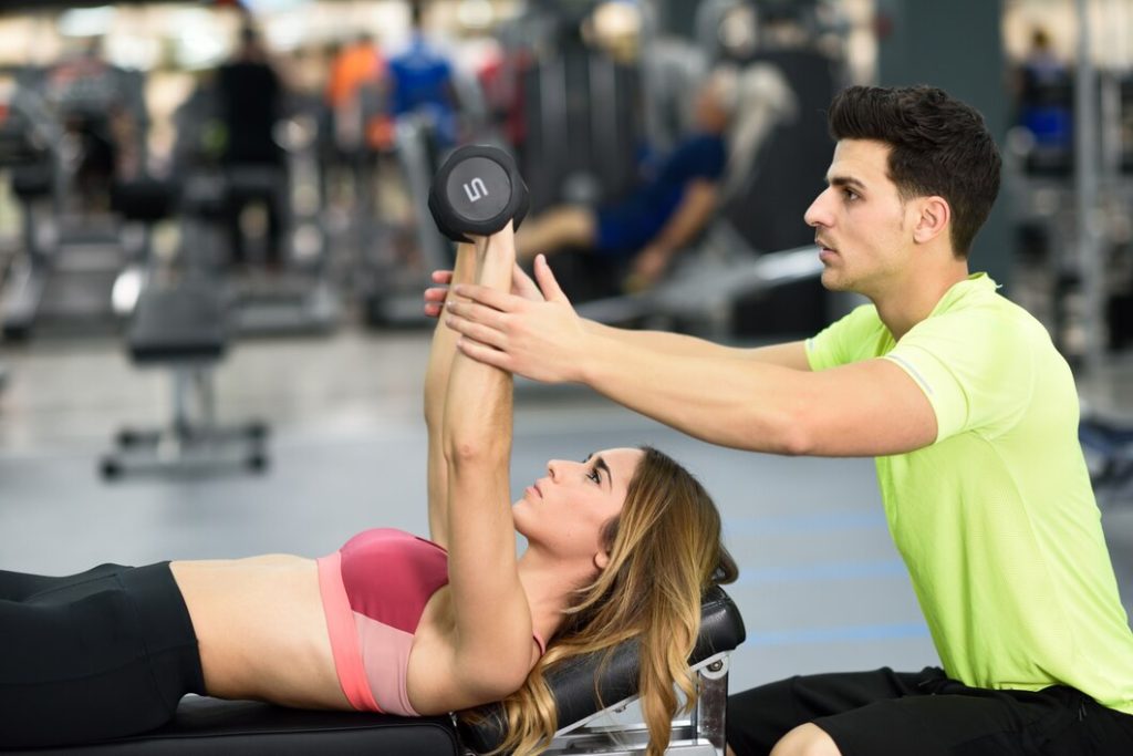 Personal trainer guiding a woman with dumbbell press workout at Congleton gym UK