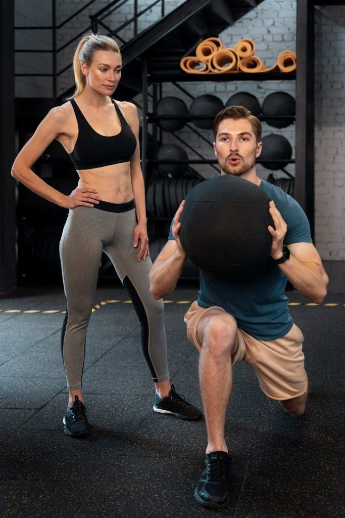 Personal trainer guiding medicine ball squat exercise in Congleton gym