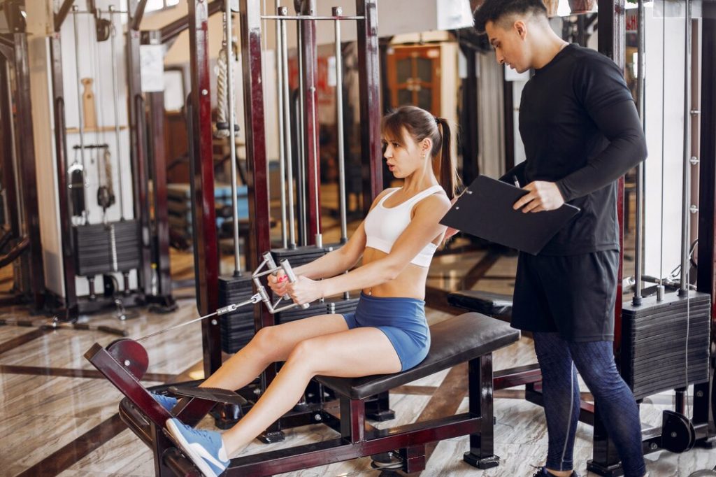 Woman performing seated row with trainer supervision in Congleton gym