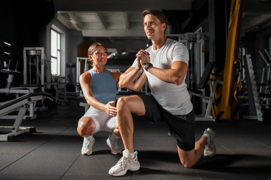 A personal trainer at a Congleton gym providing 1-on-1 form coaching for a male client performing lunges.