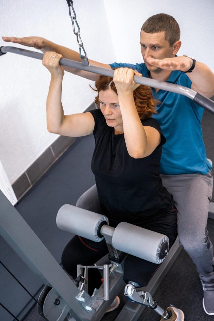 Woman doing lat pulldown exercise with personal trainer support at Congleton gym in the UK