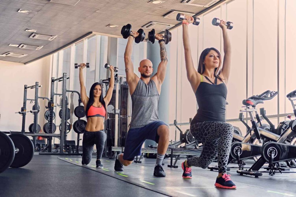 Group fitness class in Congleton gym doing dumbbell overhead lunges