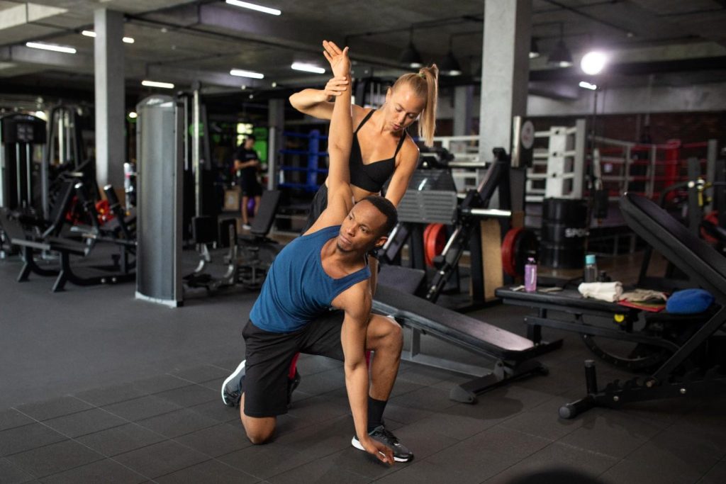 Personal trainer assisting client with stretch in Congleton gym